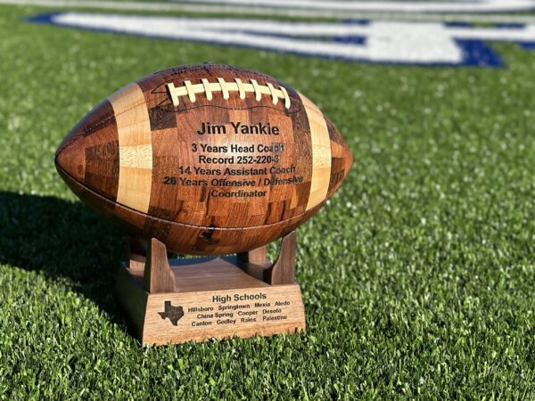 Personalized handcrafted wooden football gift with engraved base on display stand.