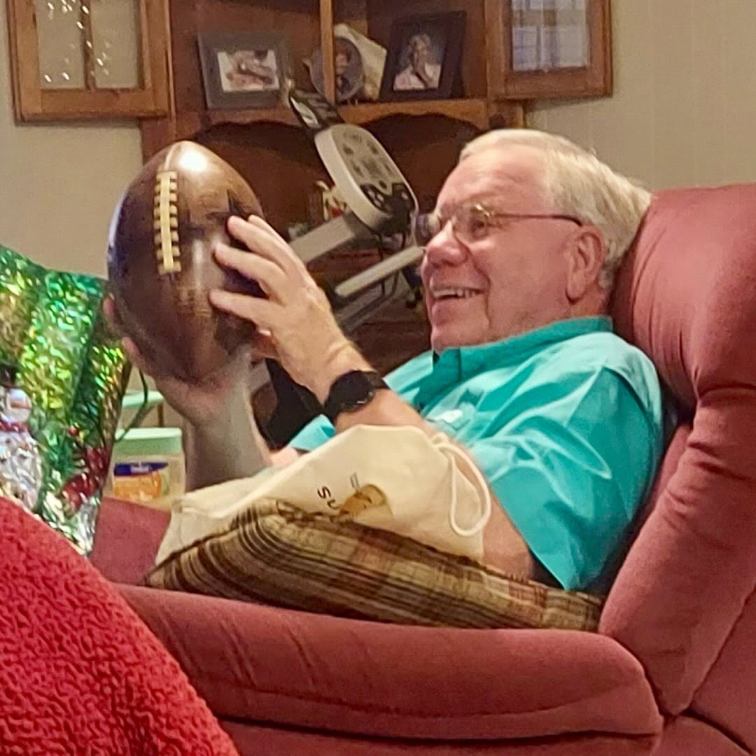 Recipient smiling while holding a handcrafted wooden football gift made from hardwood and personalized as a keepsake.